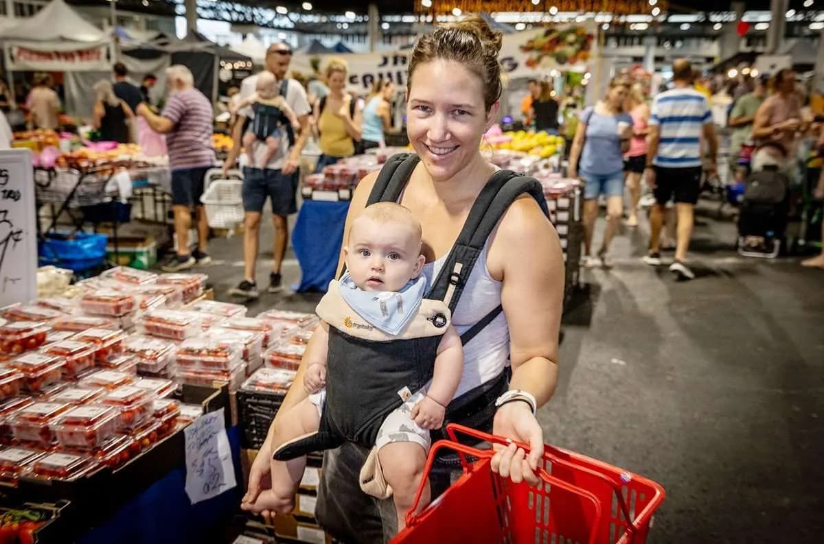 A shopper carrying a baby through the Saturday Fresh Market in Rocklea