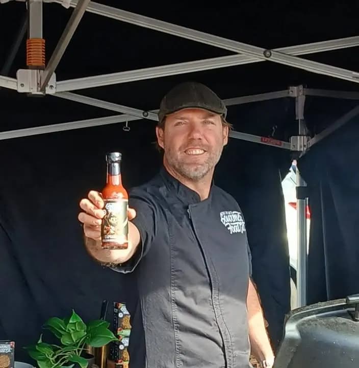 A stallholder holding up a bottle of sauce at Manly Creative Market