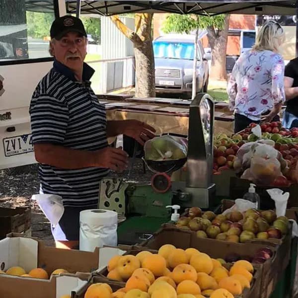 A stallholder weighing fruit beside boxes of stone fruit