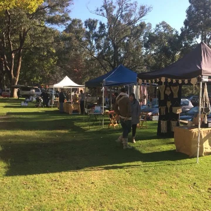 Stalls on the grass under tall trees at the Bridgetown River Market